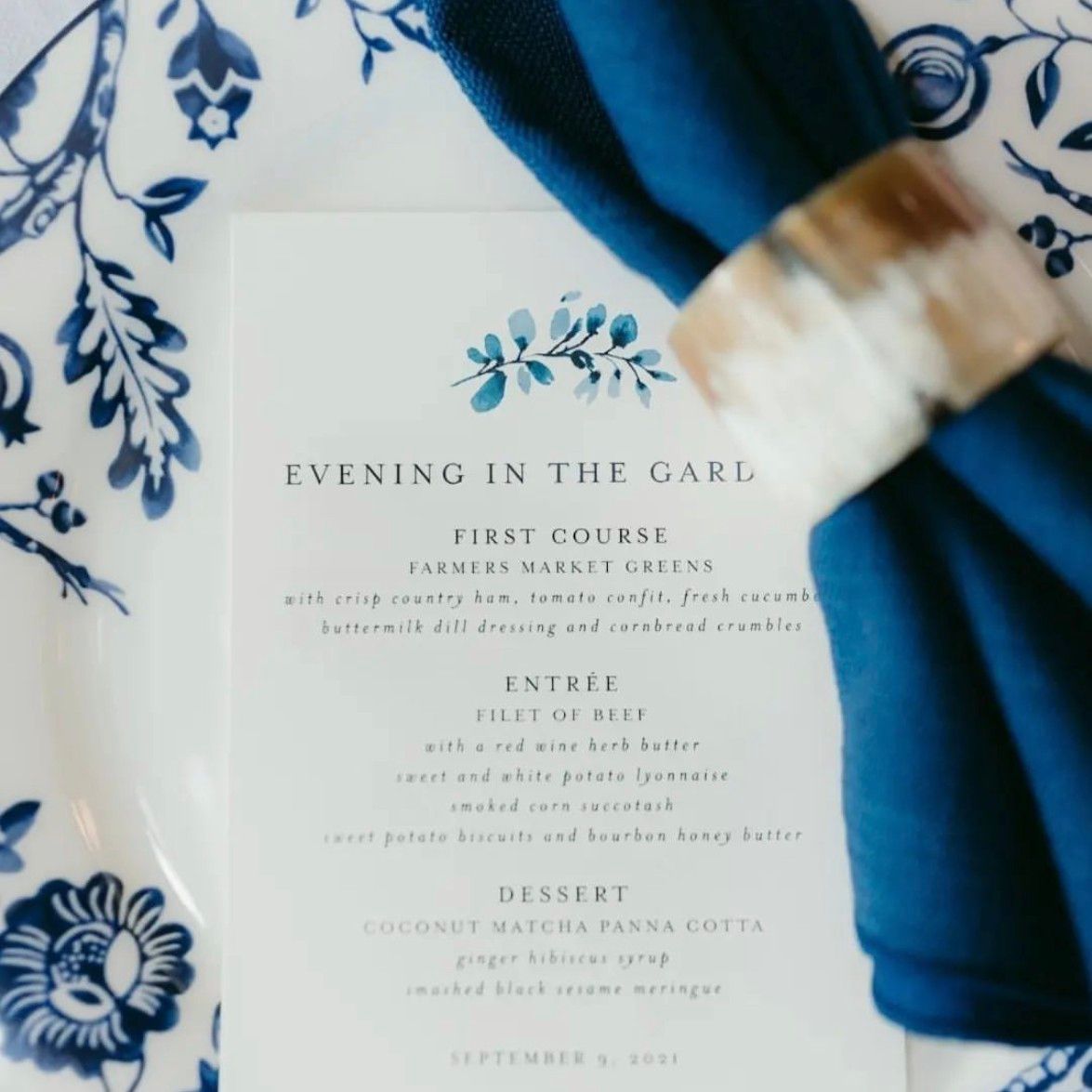 Wedding menu on a floral plate, with a blue napkin and ring. The menu is titled 