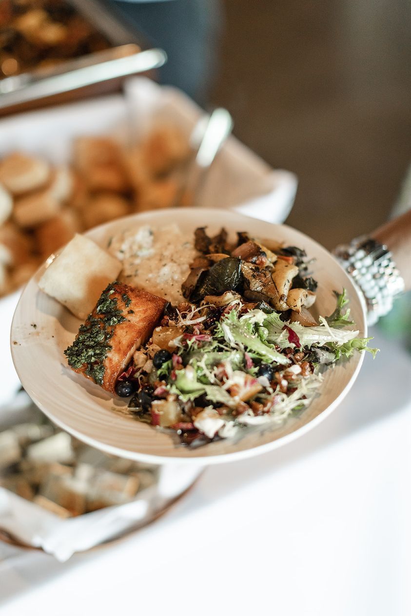 A plate of food held by a person. It includes salmon, rice, vegetables, and salad.