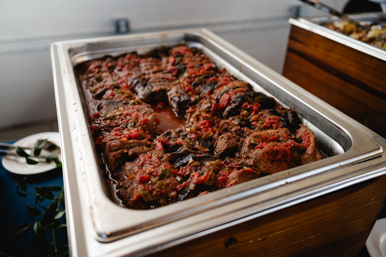 Catered dish of braised meat in a red tomato sauce, inside a stainless steel warming tray.