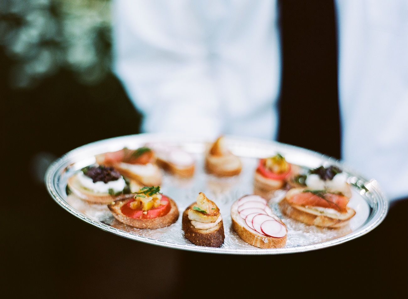 Waiter holding a silver platter with various appetizers, including toast topped with salmon, radish slices, and caviar.