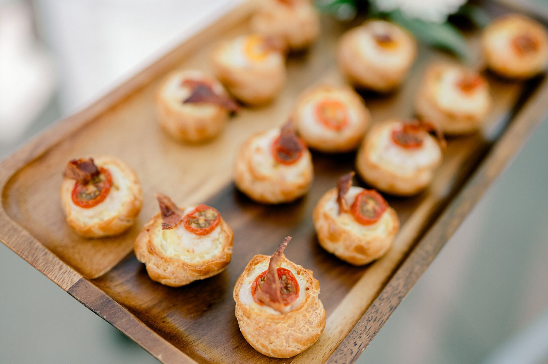 Wooden tray holding a selection of savory puff pastry appetizers, each topped with tomato and cheese.