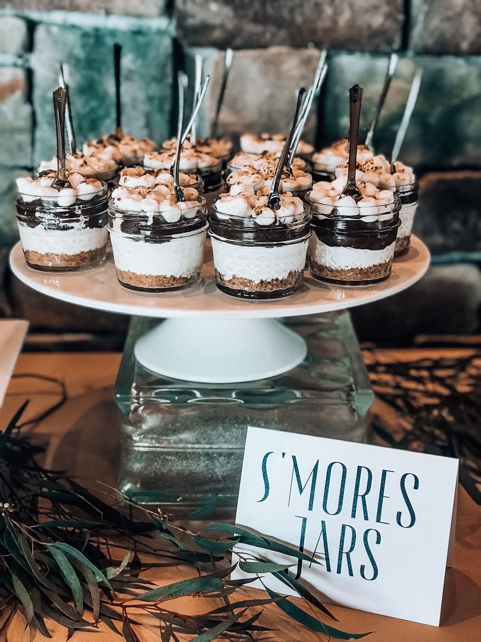 S'mores jars on a white cake stand with a sign that says 