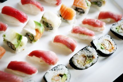 Sushi platter with nigiri and maki rolls, featuring tuna, salmon, and avocado, arranged on a white plate.