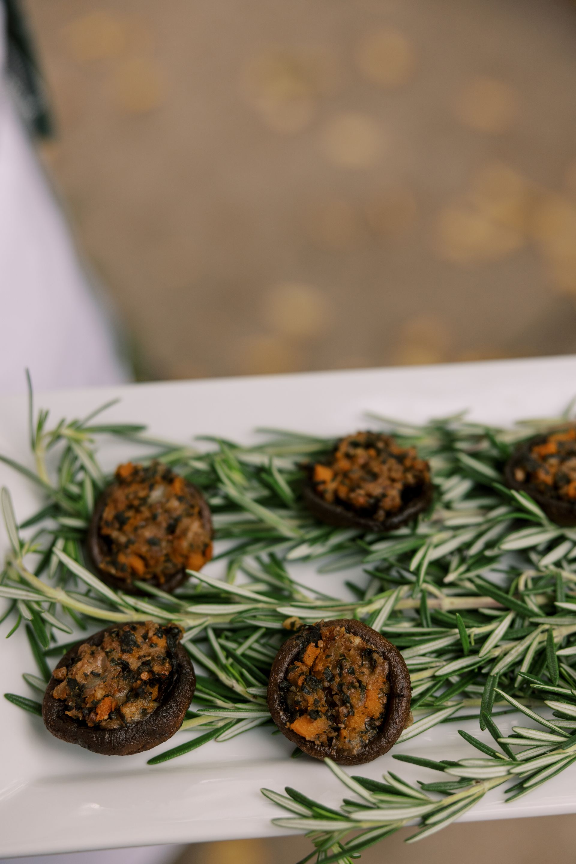 Stuffed mushrooms on a white platter, garnished with rosemary sprigs, held by a person.