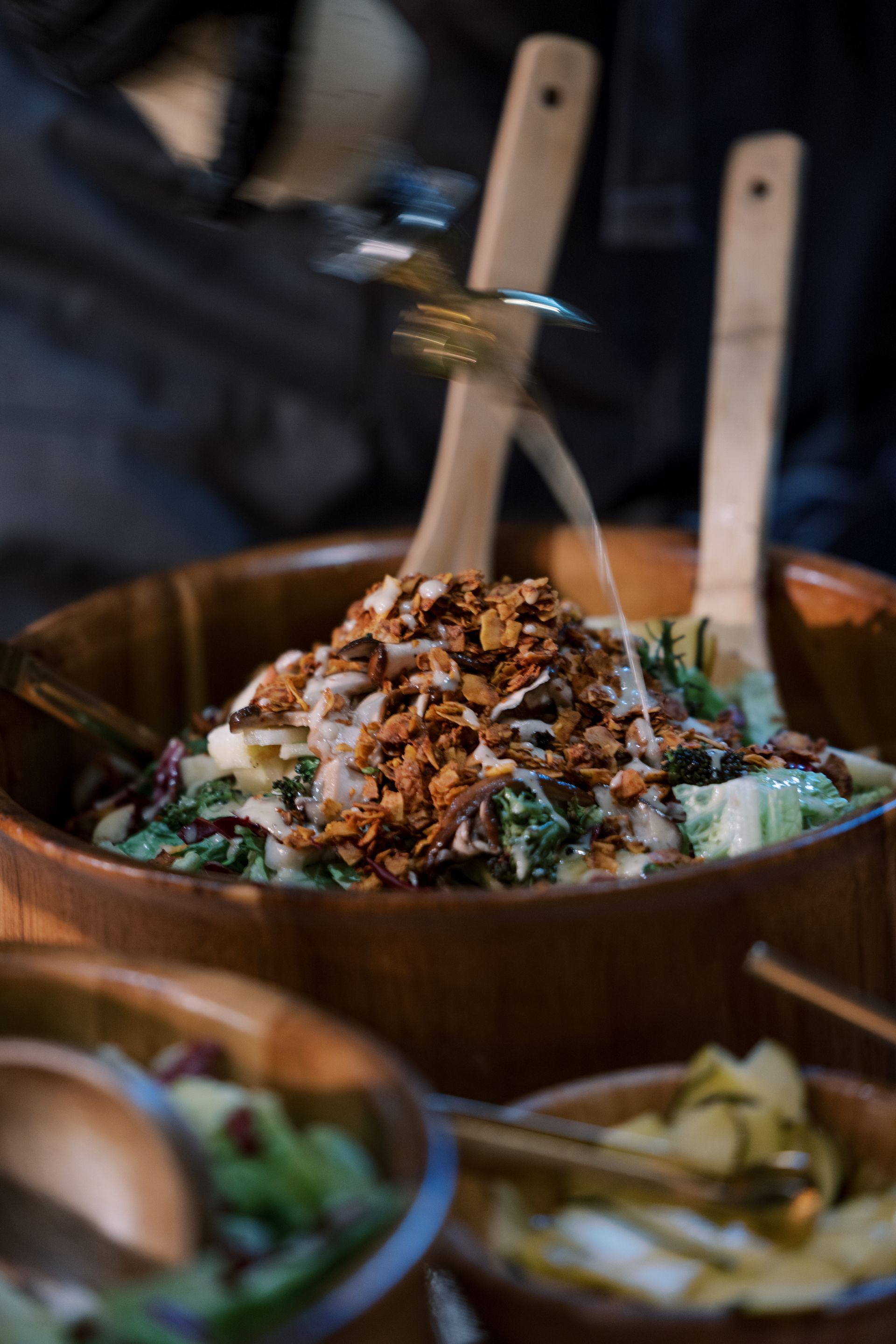 Wooden bowls of salad, topped with croutons. A person is using a fork to serve.
