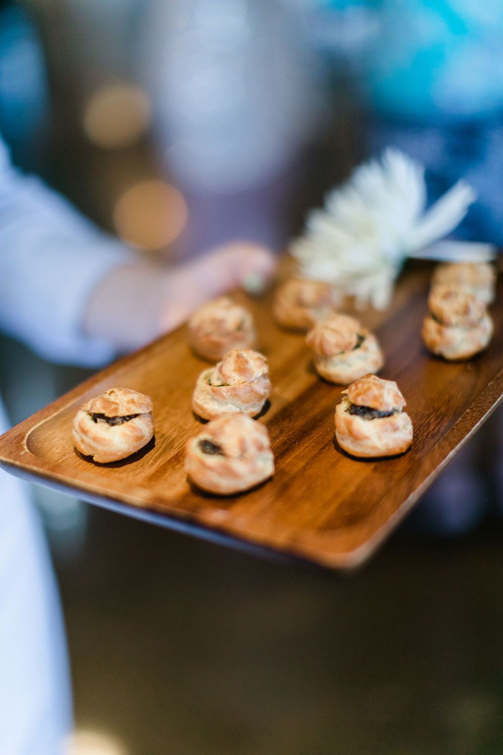 Wooden tray holding miniature pastries, possibly filled, being presented.