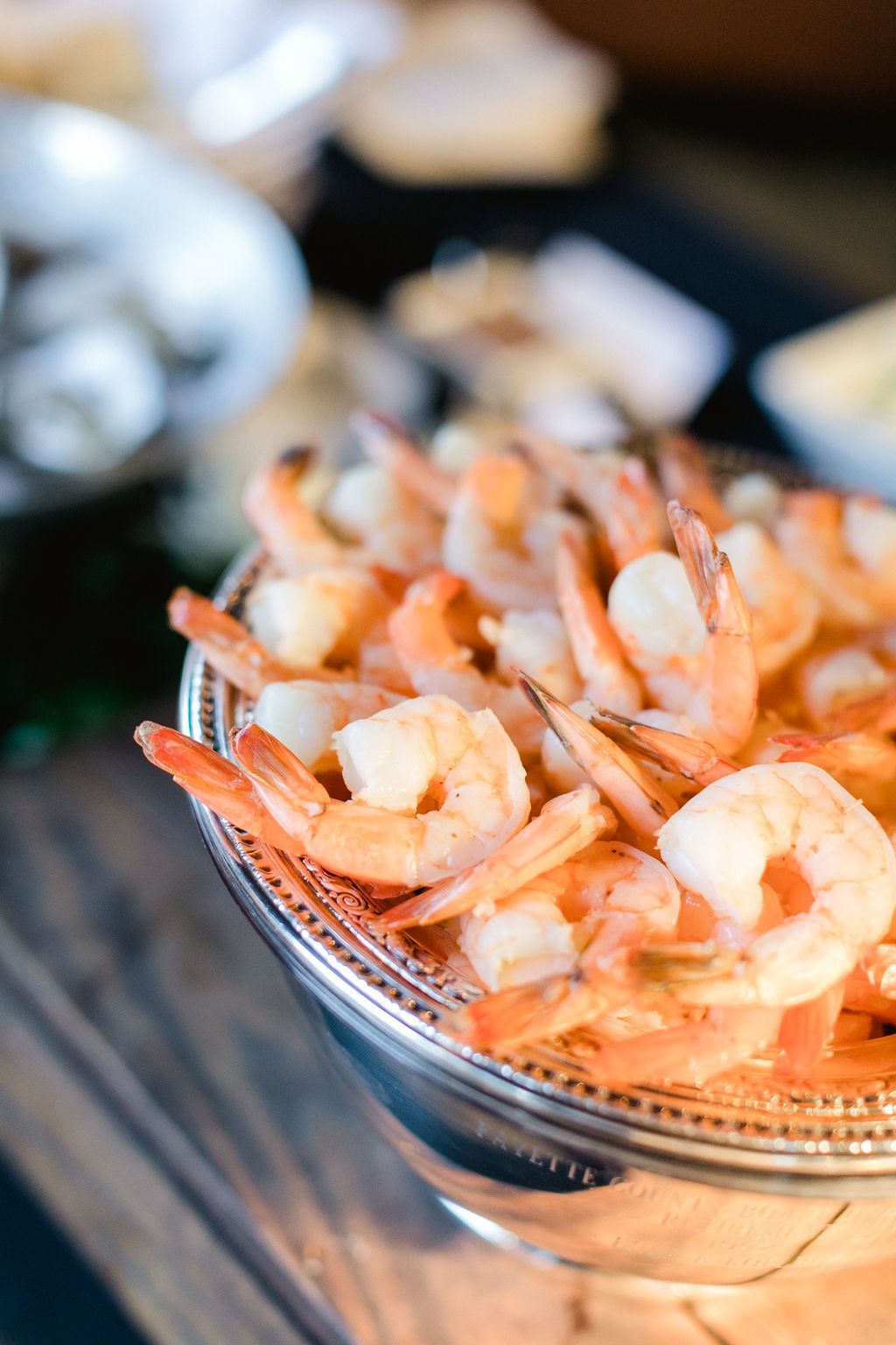 Bowl of cooked shrimp, orange-pink in color, in a silver serving dish, part of a buffet spread.