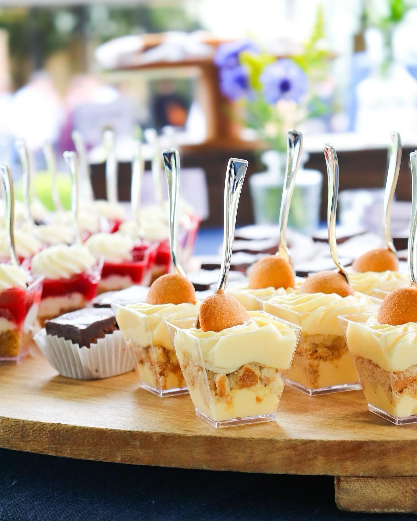Dessert display with small, clear cups of layered desserts, including banana pudding and parfaits, served with spoons.