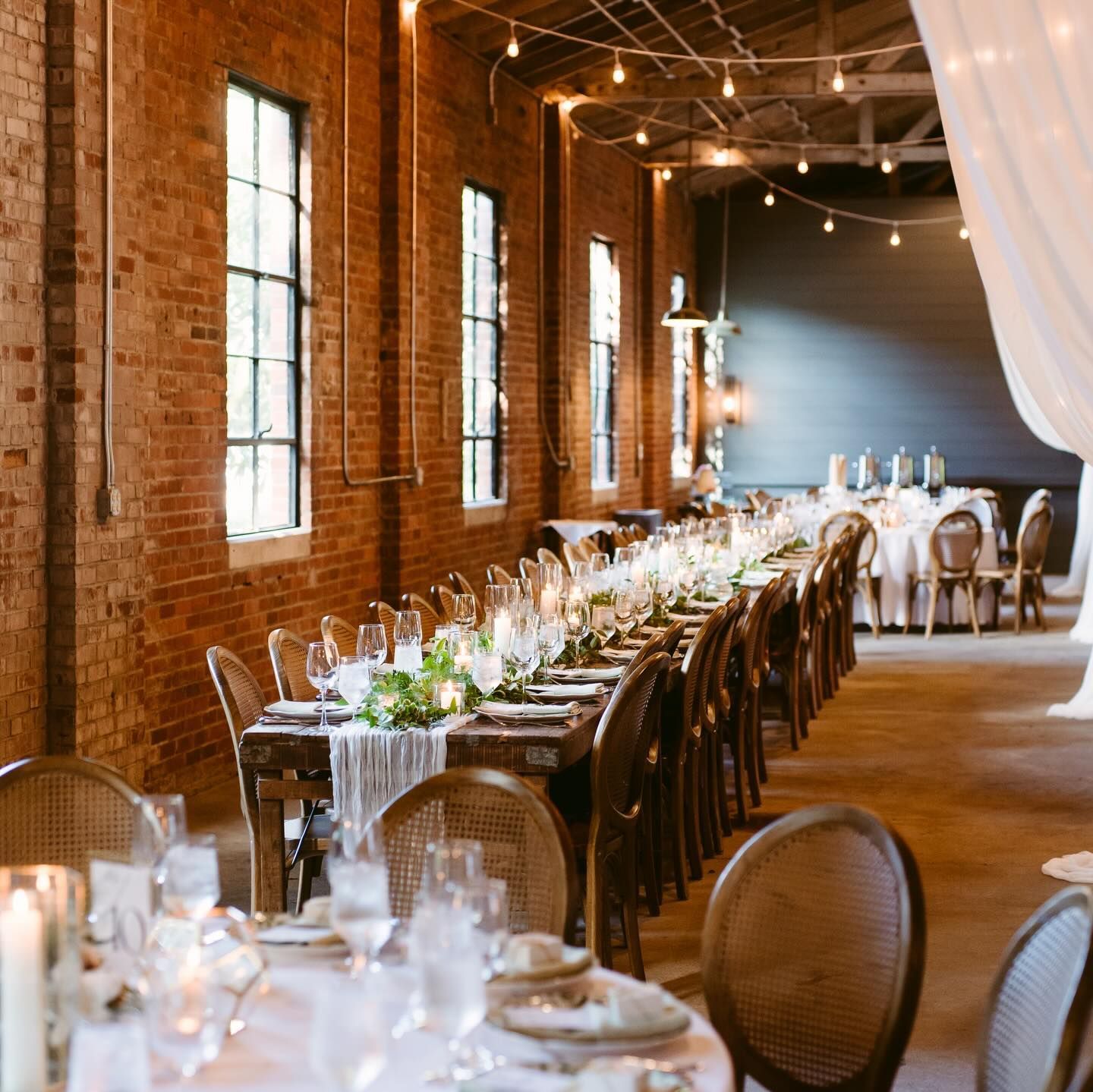 Elegant wedding reception with long table, brick walls, and string lights.