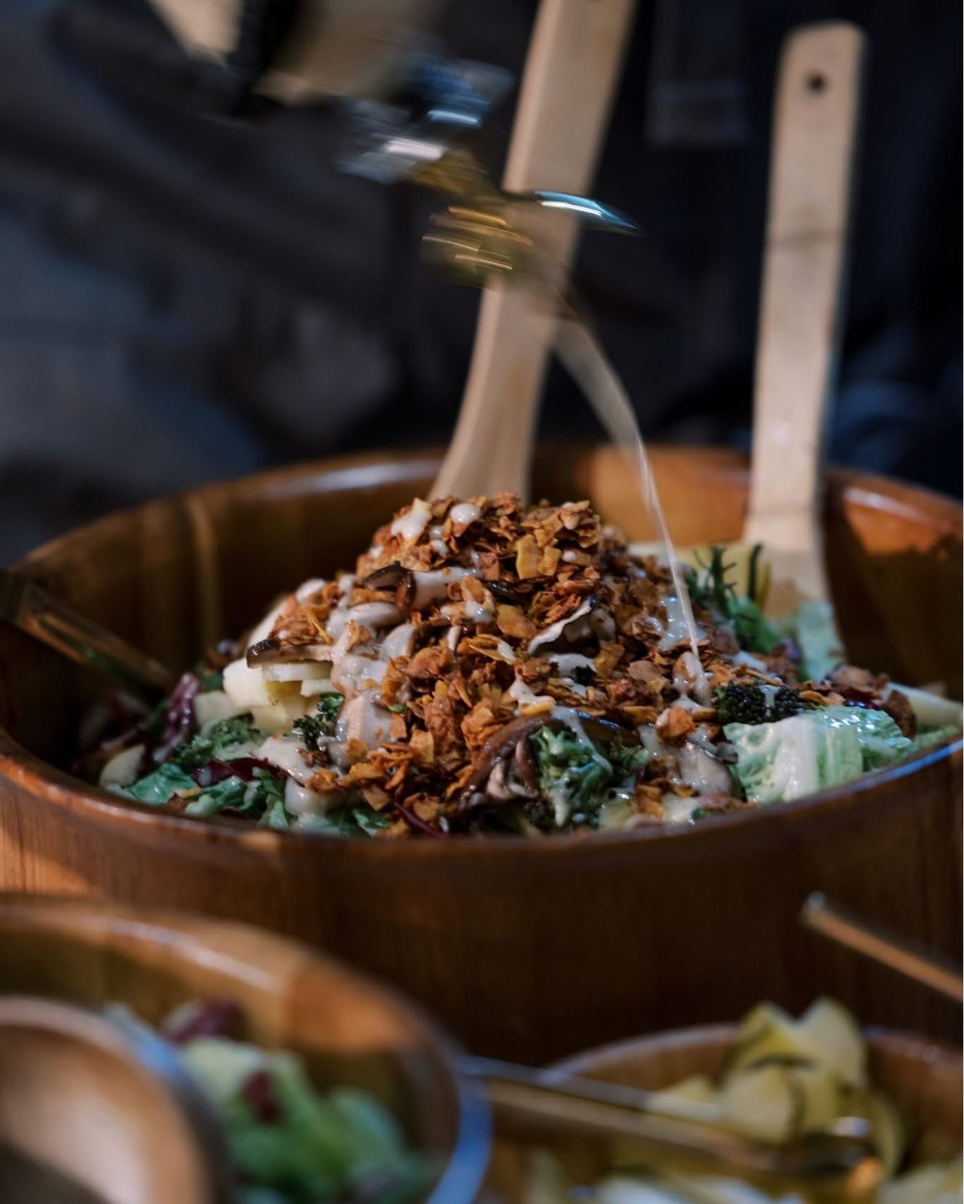 Wooden bowl of salad with toppings being added.