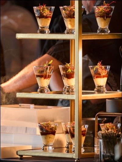 Appetizers in glass cups on a tiered gold stand, being prepared.