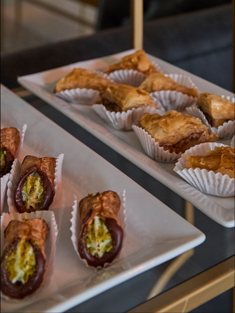 Two white platters with assorted pastries, including cannoli and baklava.