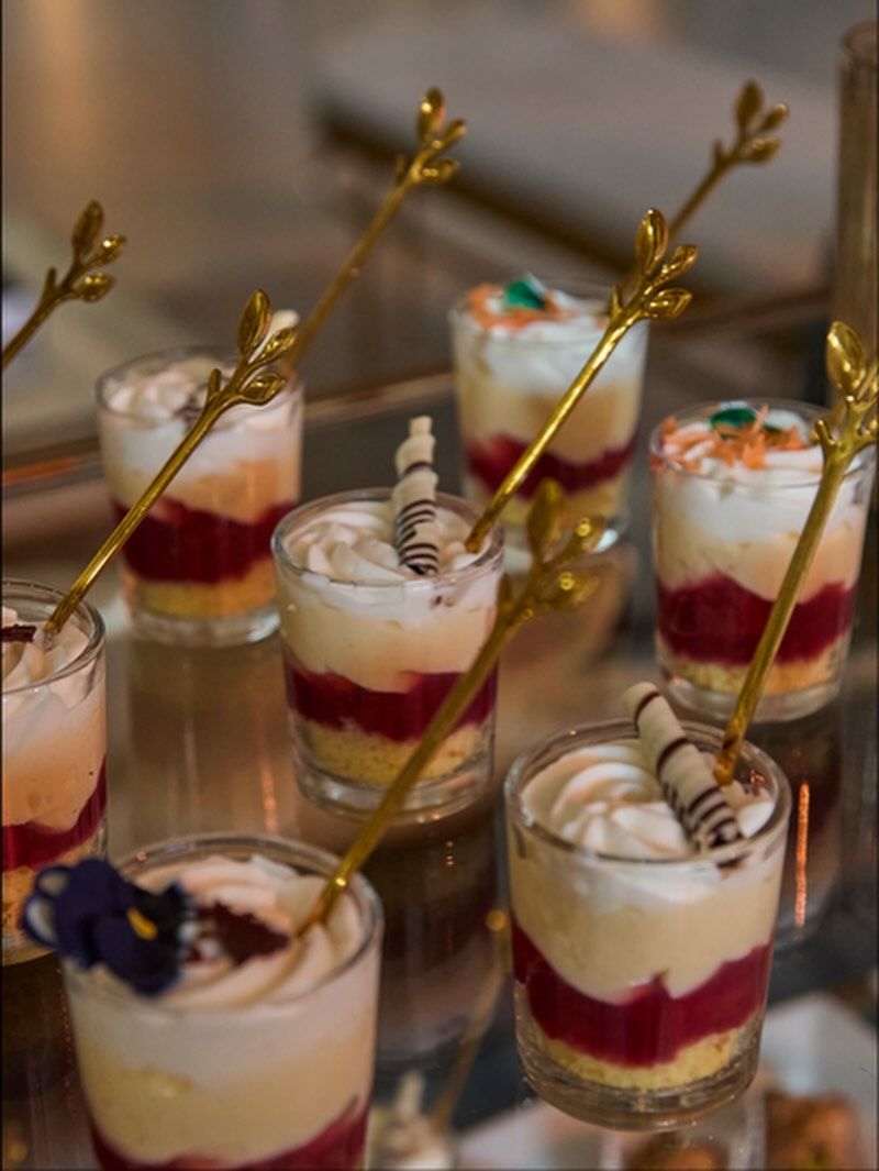 Dessert parfaits in small glasses with gold spoons. Layered with cake, berries, and whipped cream.