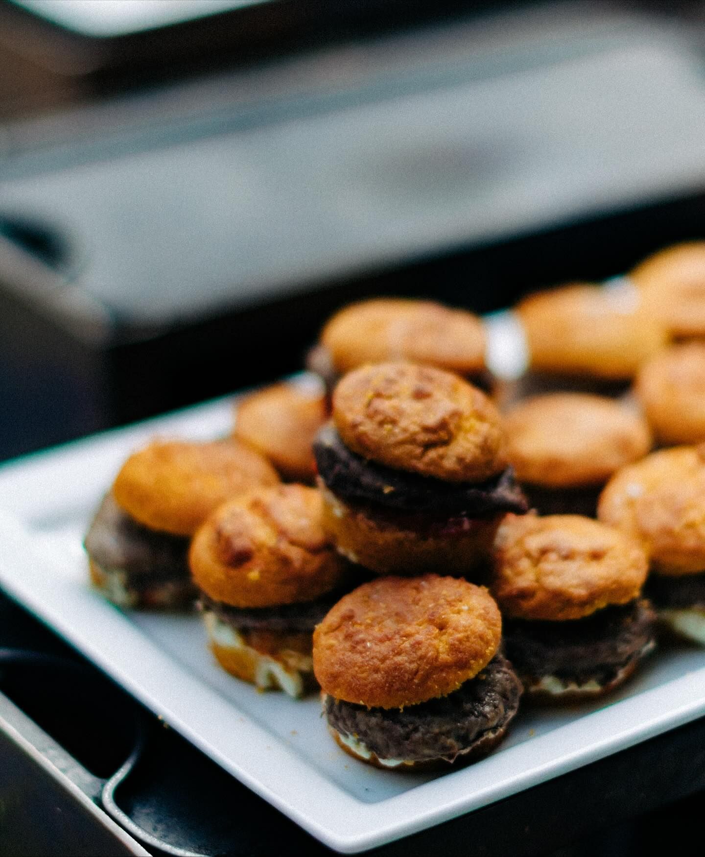 Miniature burgers on a white square plate, on a dark surface.