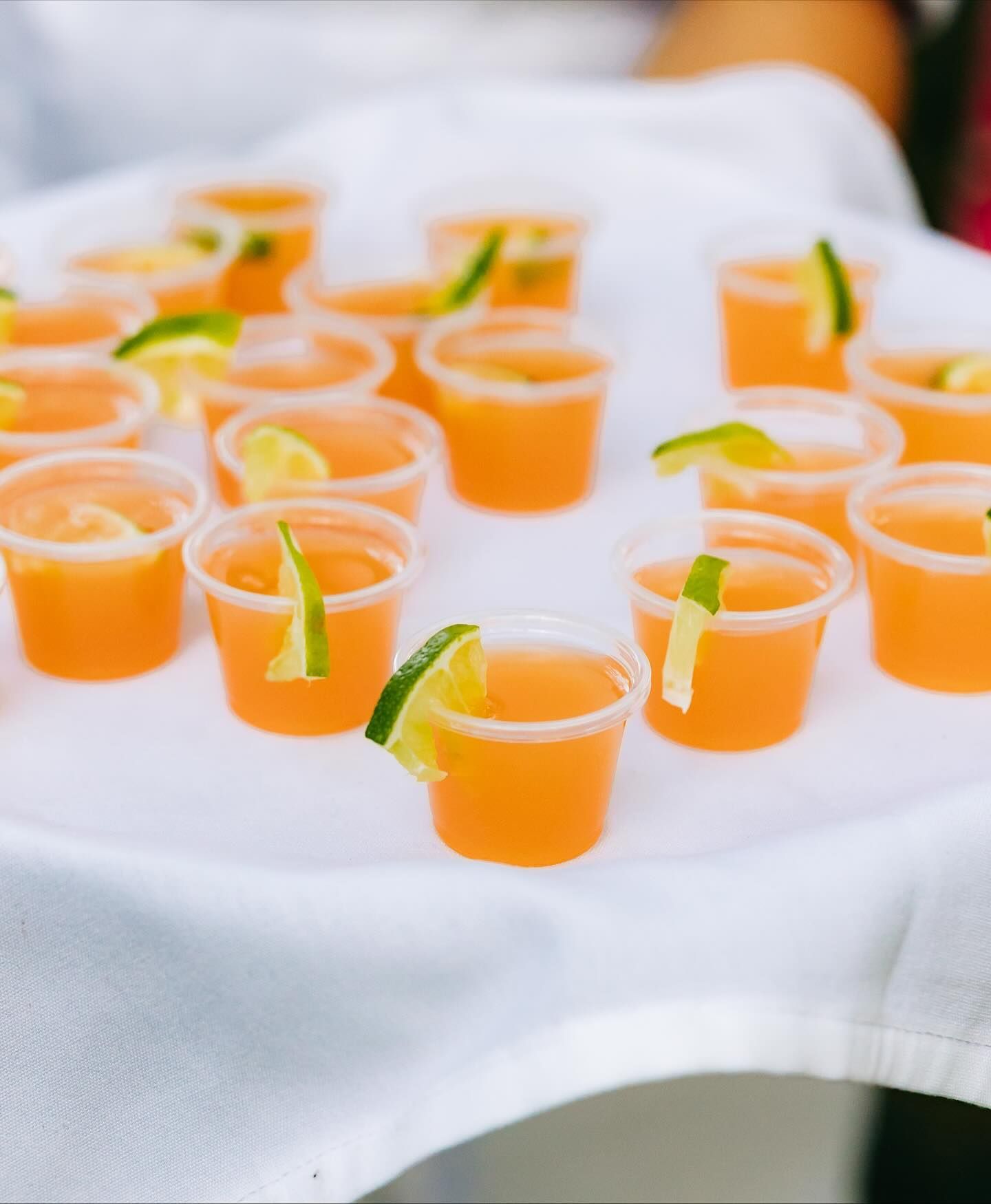 Tray of orange cocktails in clear cups, garnished with lime slices, on a white cloth.