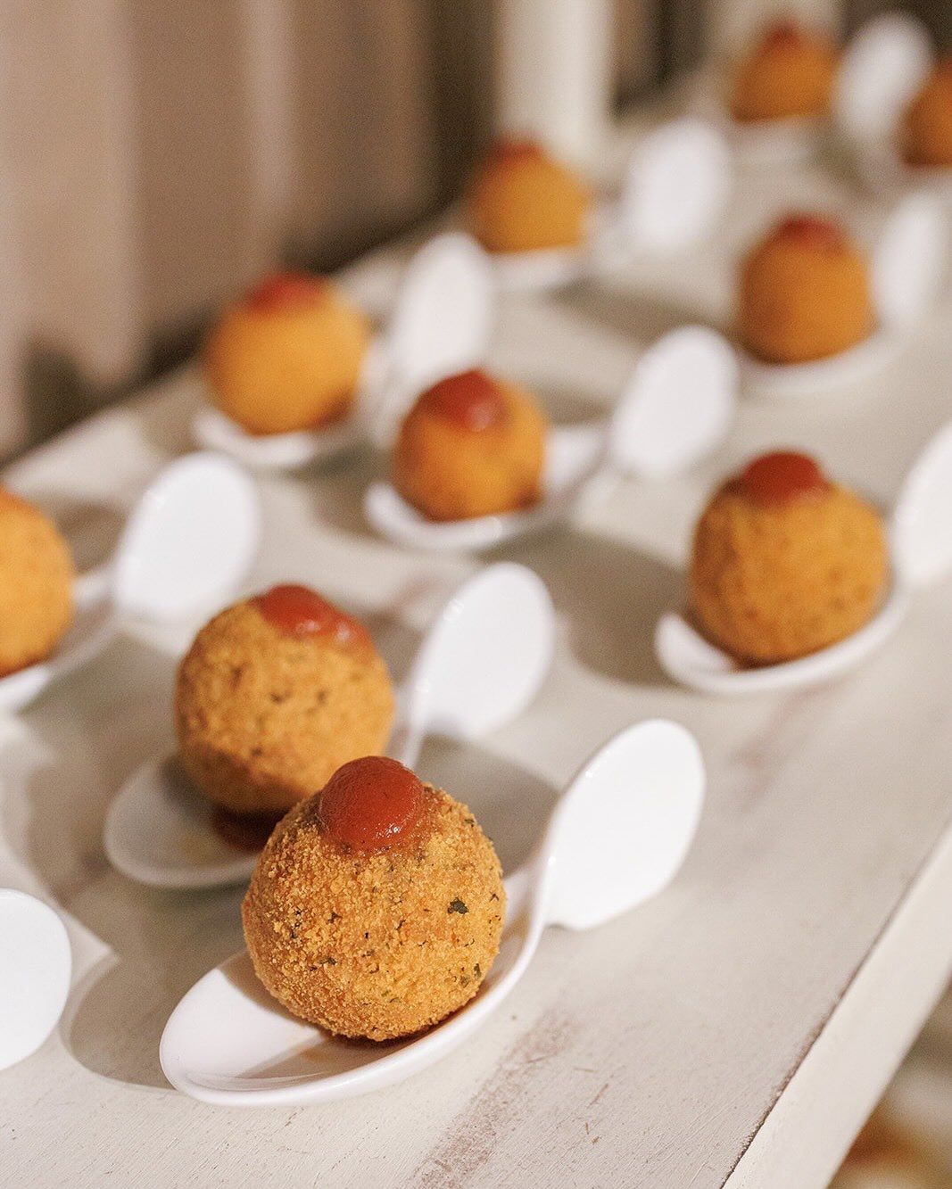 Golden, fried appetizers topped with red sauce, served on white spoons.