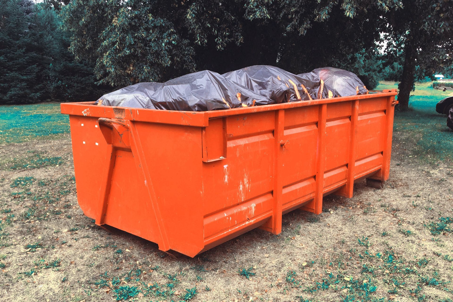 Blue dumpster in front of a house under construction; wooden frame and lumber visible.
