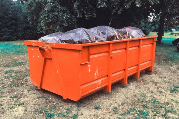 Orange dumpster filled with black trash bags outdoors on grass.