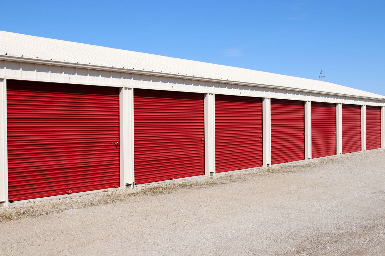 Red storage unit doors under a white roof against a blue sky.