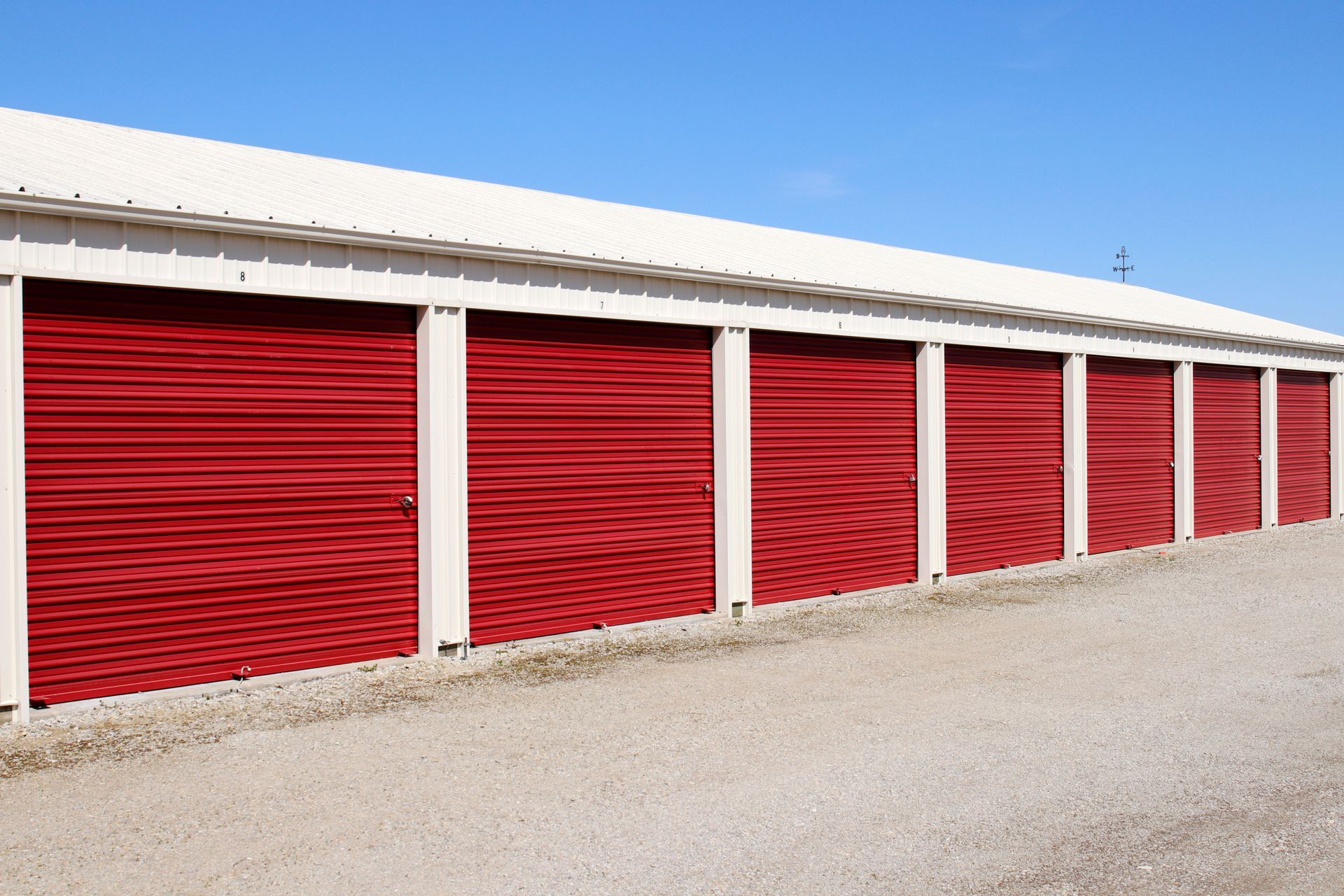 Red storage unit doors under a white roof against a blue sky.