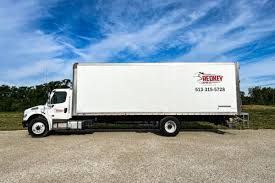 White moving truck on pavement under a blue sky with scattered clouds. Truck has company logo on the side.
