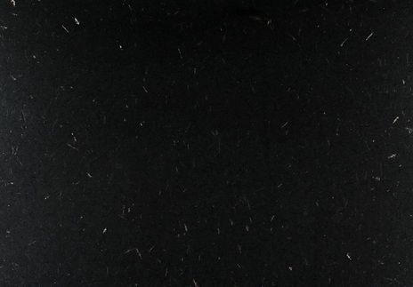 Dark, textured black surface with scattered white specks and thin lines.