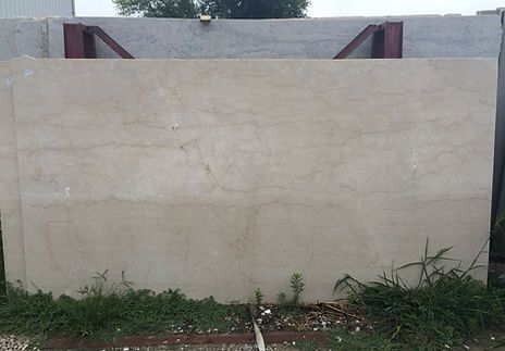 Large slab of light beige stone, displayed outdoors, supported by metal beams.