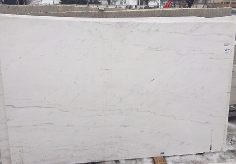 A large white marble slab with light gray veining, stacked outside on pallets.