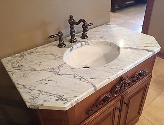 Vanity with a marble countertop and oval sink, set in a brown cabinet with decorative carvings.