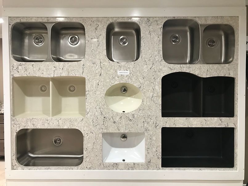 Display of various kitchen sinks in a showroom, mounted on a speckled countertop surface.