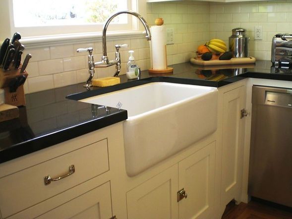Kitchen with white farmhouse sink, black countertop, stainless steel faucet, cabinets, and appliances.
