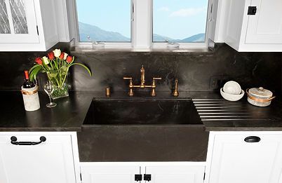 Black farmhouse sink in a kitchen, with white cabinets and a view of mountains.