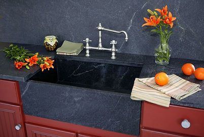 Black farmhouse sink with chrome faucet, orange lilies, and oranges on a red kitchen counter.