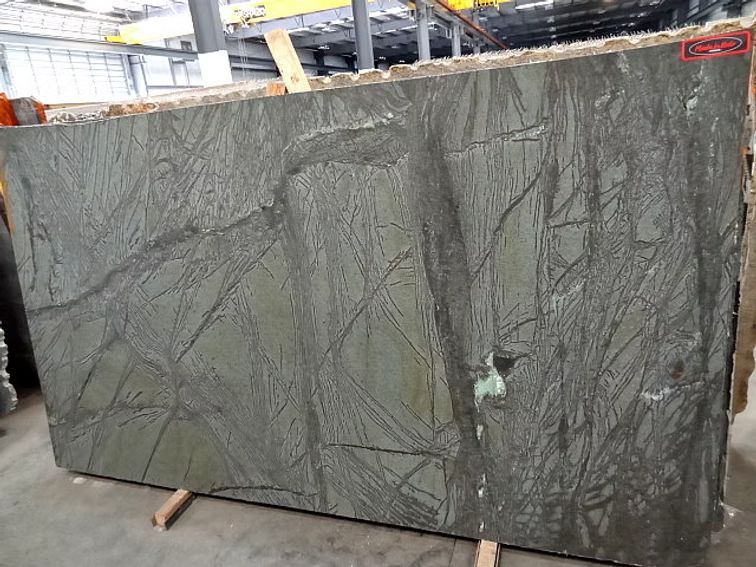 Large slab of green stone with dark veining, propped up in a warehouse setting.