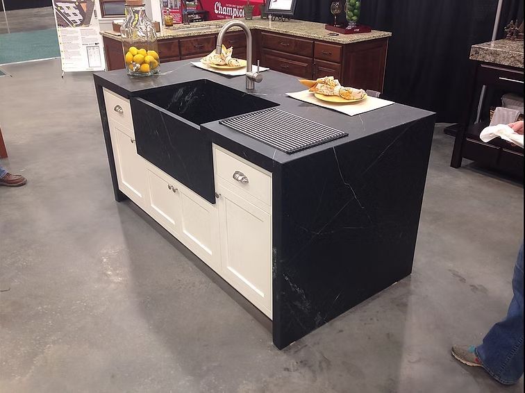 Kitchen island with black countertop, white cabinets, and a farmhouse sink.