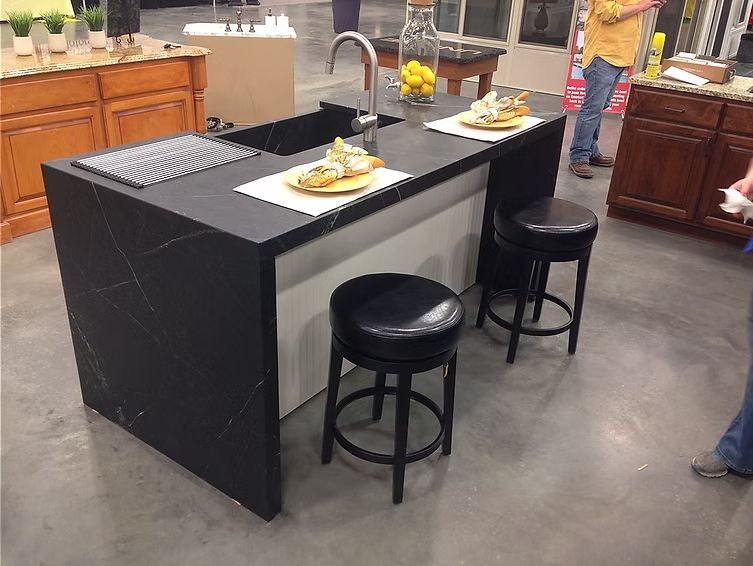 Black countertop kitchen island with sink and stools, showcasing a display.