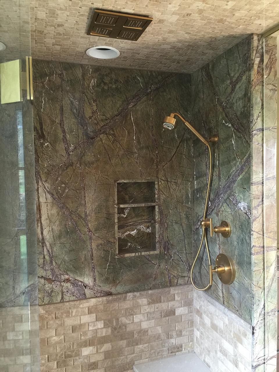 Green and brown marbled shower with gold fixtures and recessed niche.