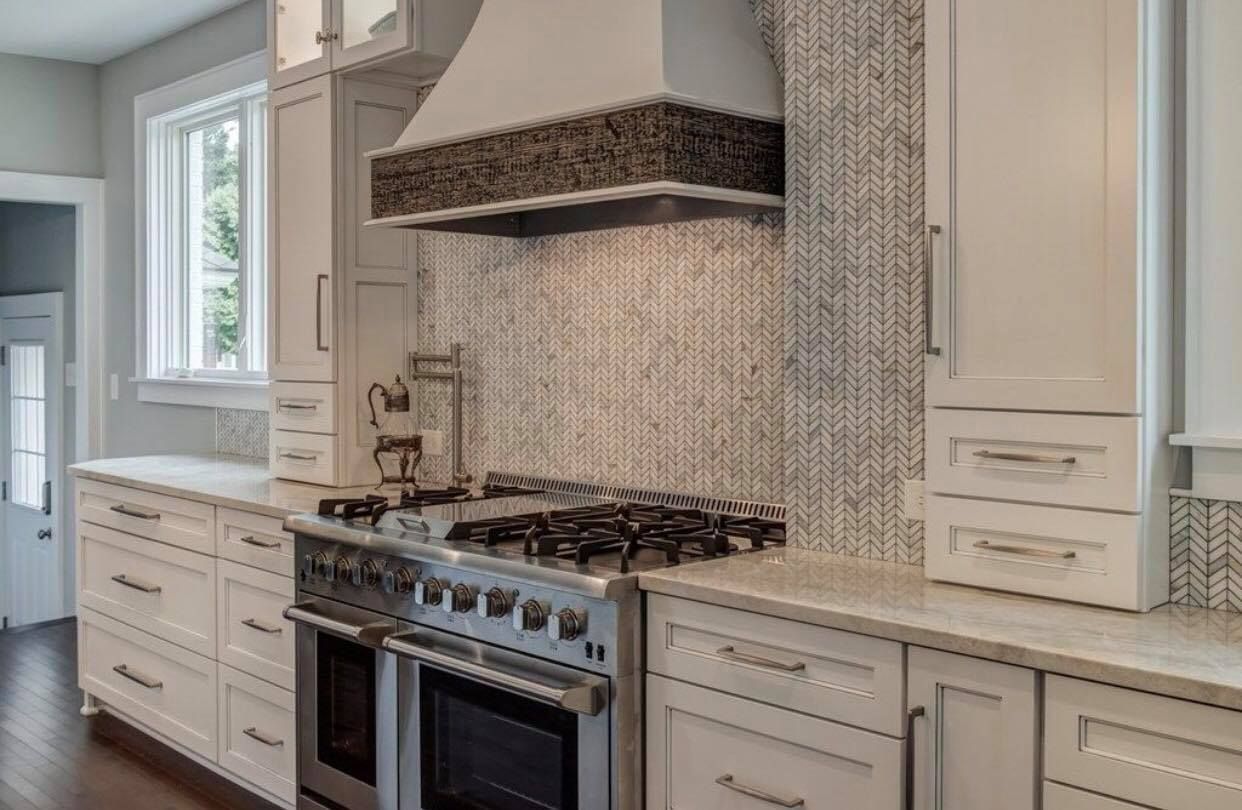White kitchen with stainless steel oven, backsplash, and range hood.
