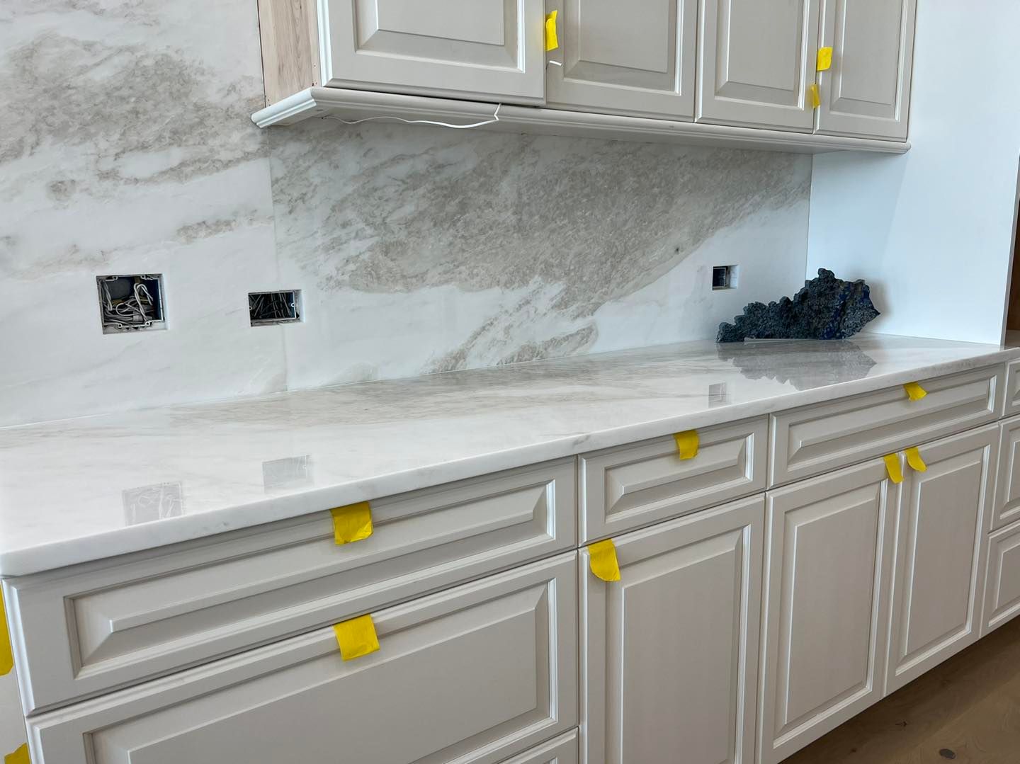 White kitchen cabinets and countertops with a marble backsplash.