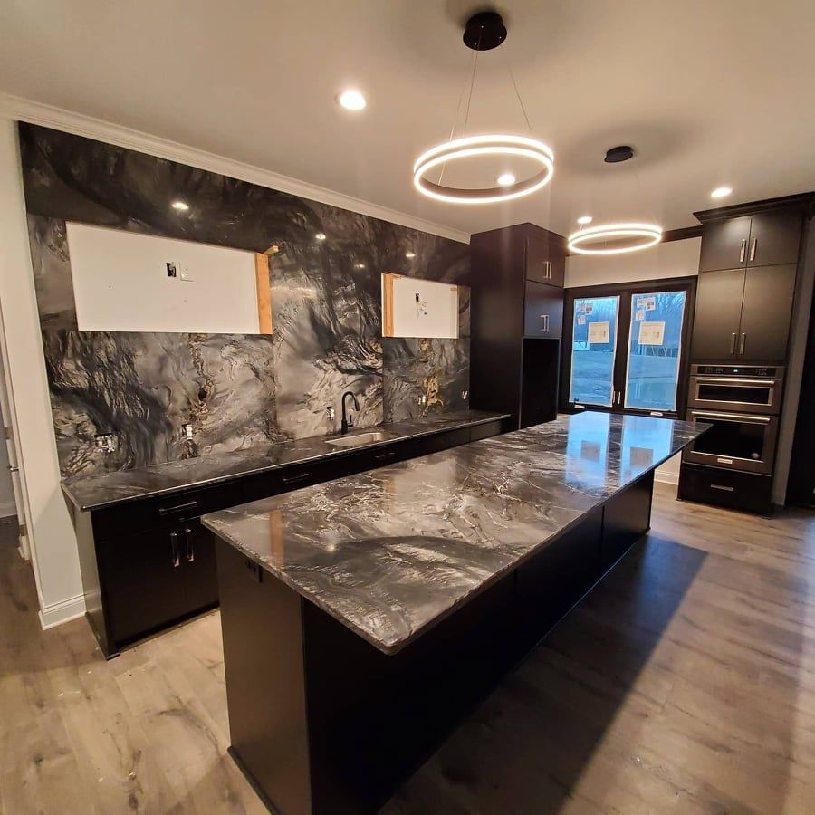 Modern kitchen with black cabinets and countertops, island, and large black marble backsplash.