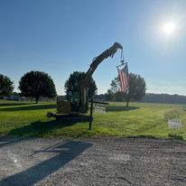 A crane is lifting an american flag in a field.