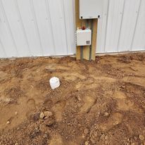 A white box is sitting in the dirt next to a fence.