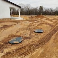 Two septic tanks are sitting in the dirt in front of a house.