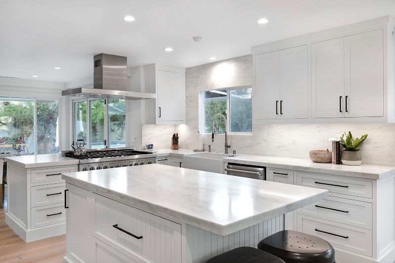 A kitchen with white cabinets , stainless steel appliances , and a large island.