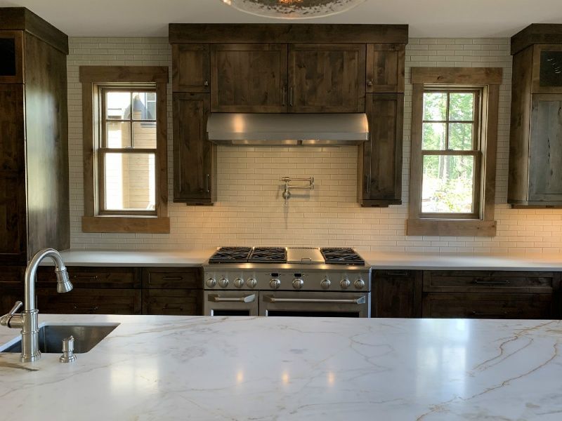 A kitchen with a stove , sink , and two windows.
