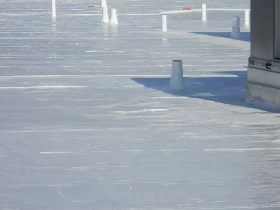 A flat, white-coated commercial roof with several small pipes and a large mechanical unit structure in the corner.