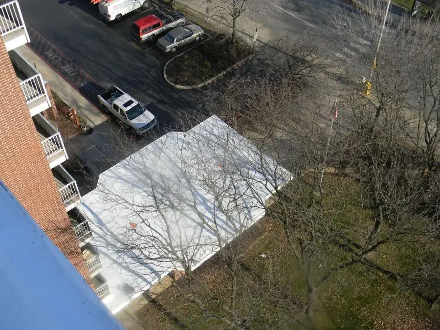High-angle view of a white, rectangular patch of snow on a parking lot next to a brick apartment building and bare trees.
