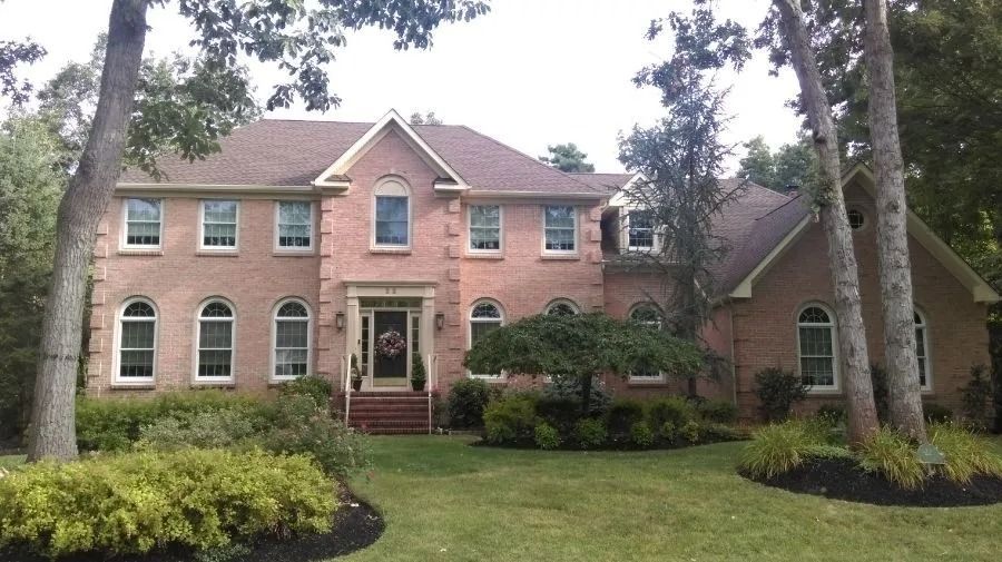 A two-story, light-colored brick house with a symmetrical front entrance and arched windows, surrounded by trees and lawn.