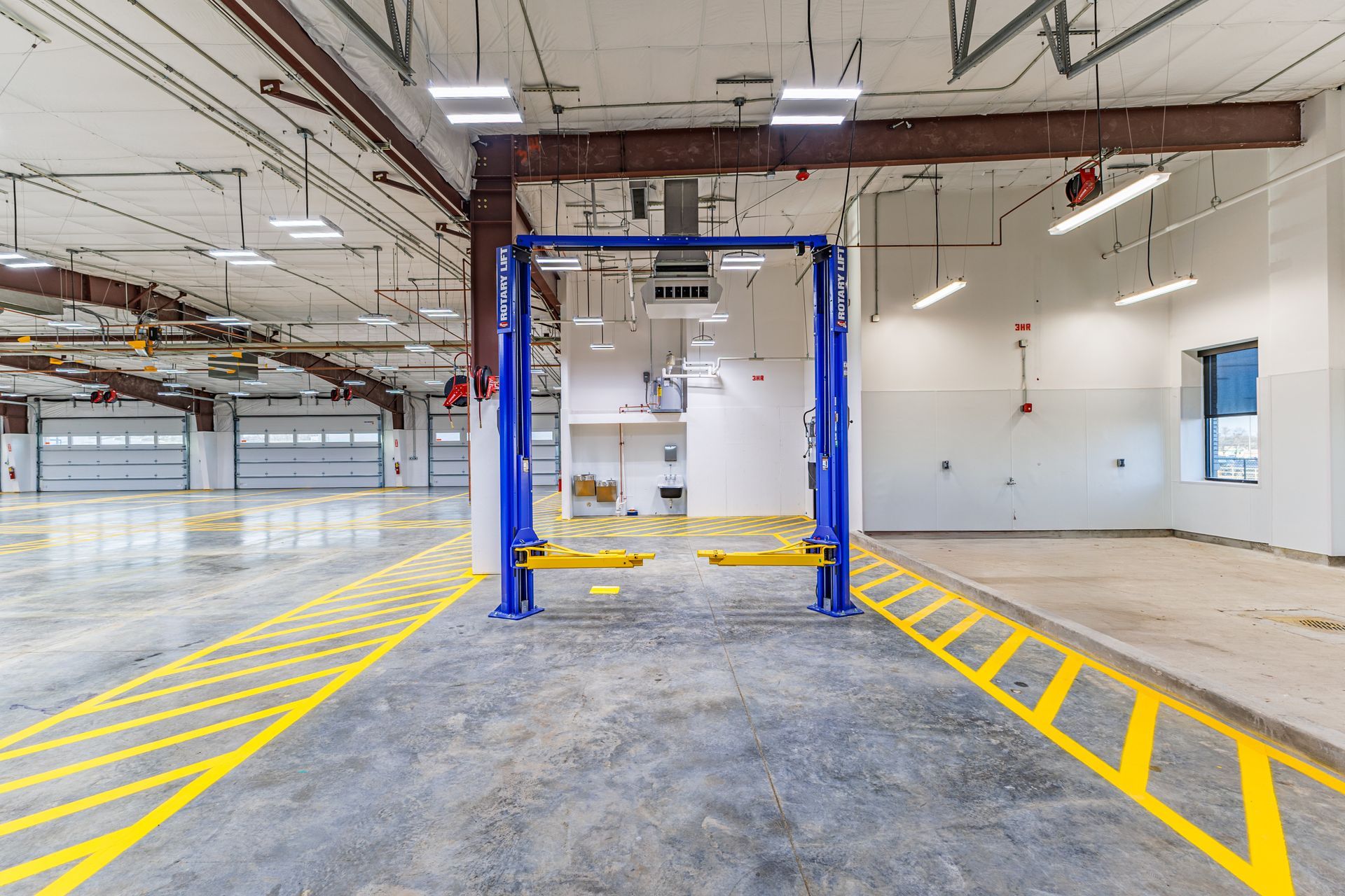Blue car lift in a large, empty garage with yellow painted lines on the floor.