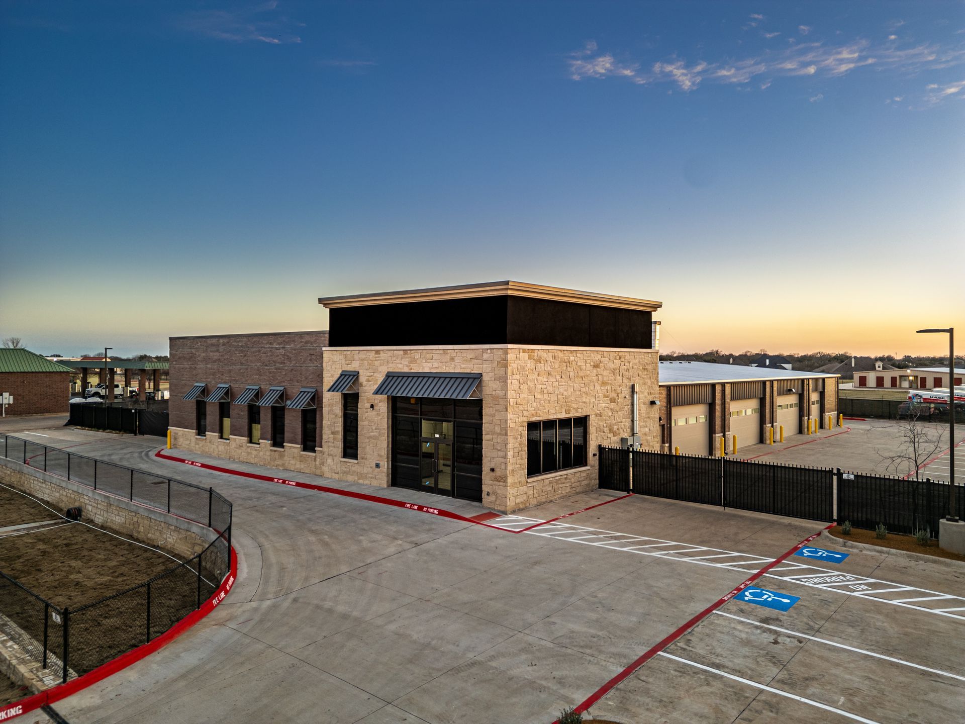 Exterior view of a brick building with storage units, asphalt parking, and a dusk sky.